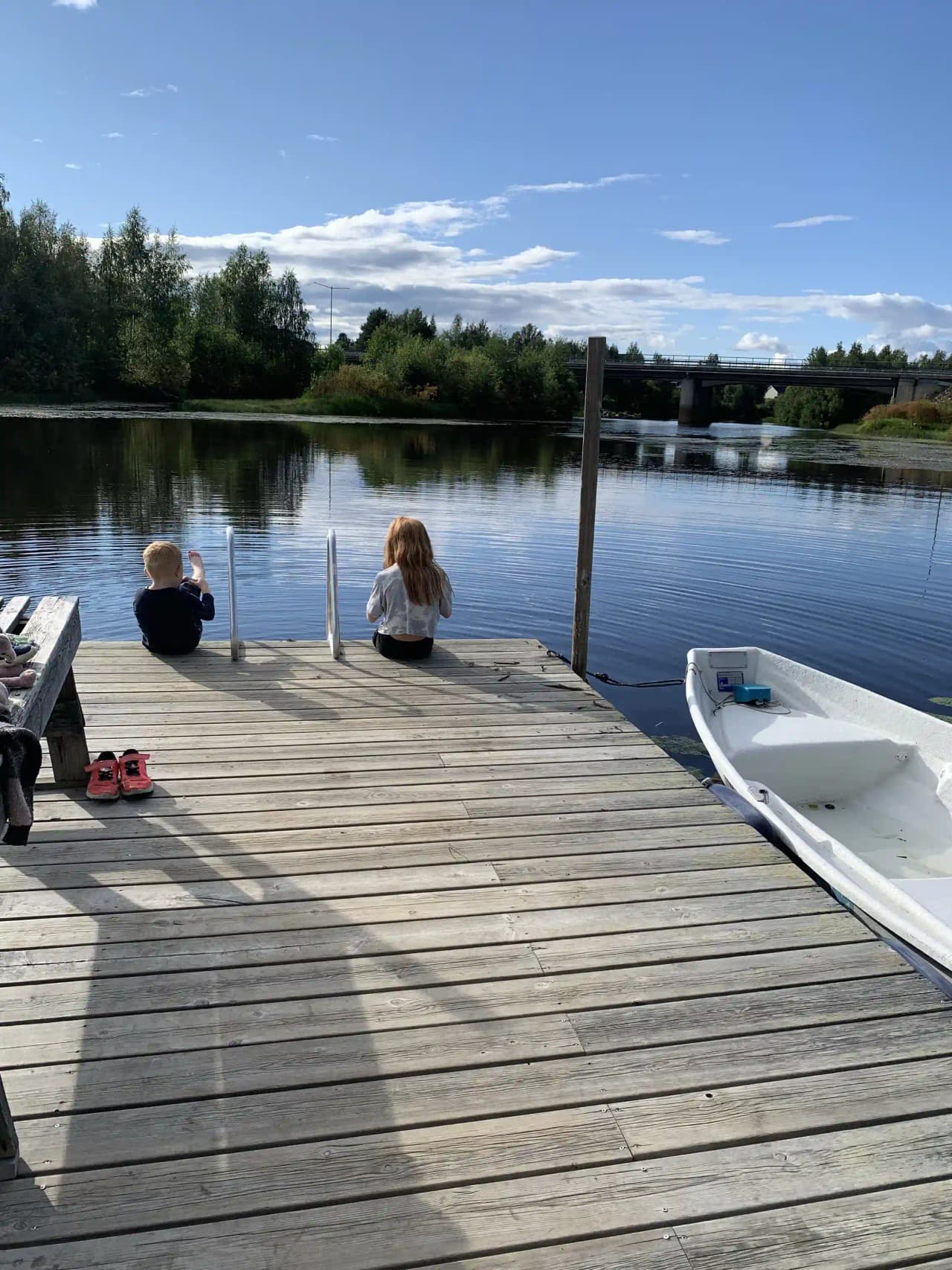 Bild av Sangis Motell och Camping med en docka som leder till en båt vid en sjö. Moln speglas i vattnet och en brygga sträcker sig ut i kanalen.
