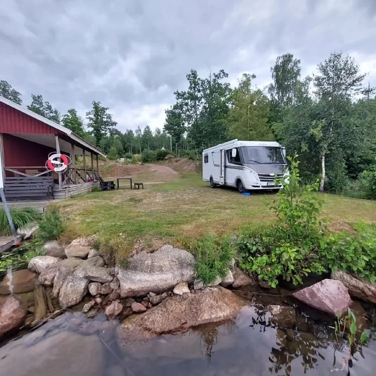 En lugn campingplats vid Stora Rödje med husvagnar och husbilar uppställda bland grönskande växtlighet, i närheten syns en liten damm.