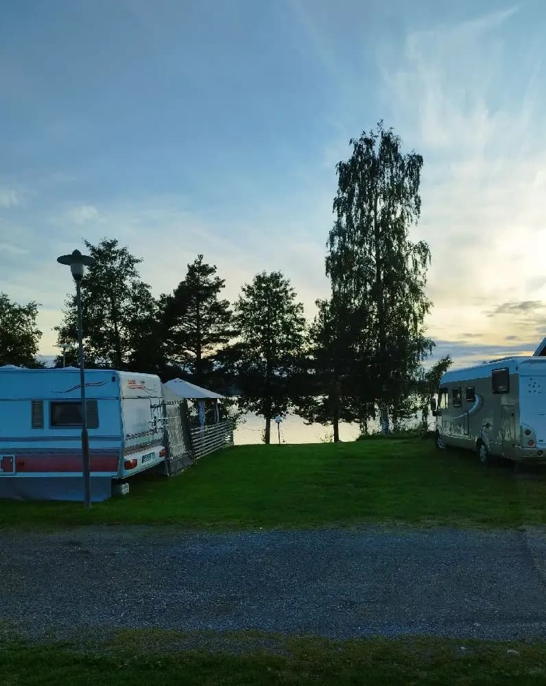 En husvagn står parkerad på en grön gräsmatta vid Säters camping, omgiven av ett par tält i skymningen.