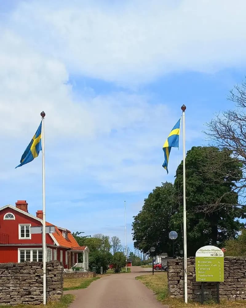 En flagga vajar på en flaggstång över en grön gräsmatta, med en klar himmel i bakgrunden vid Allégården Kastlösa.