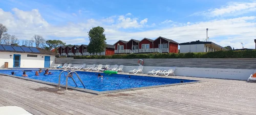 Bild av Allégården Kastlösa: En utomhuspool med omgivande solstolar och parasoll, omges av lugnande grönska vilket ger platsen en avkopplande resortkänsla.