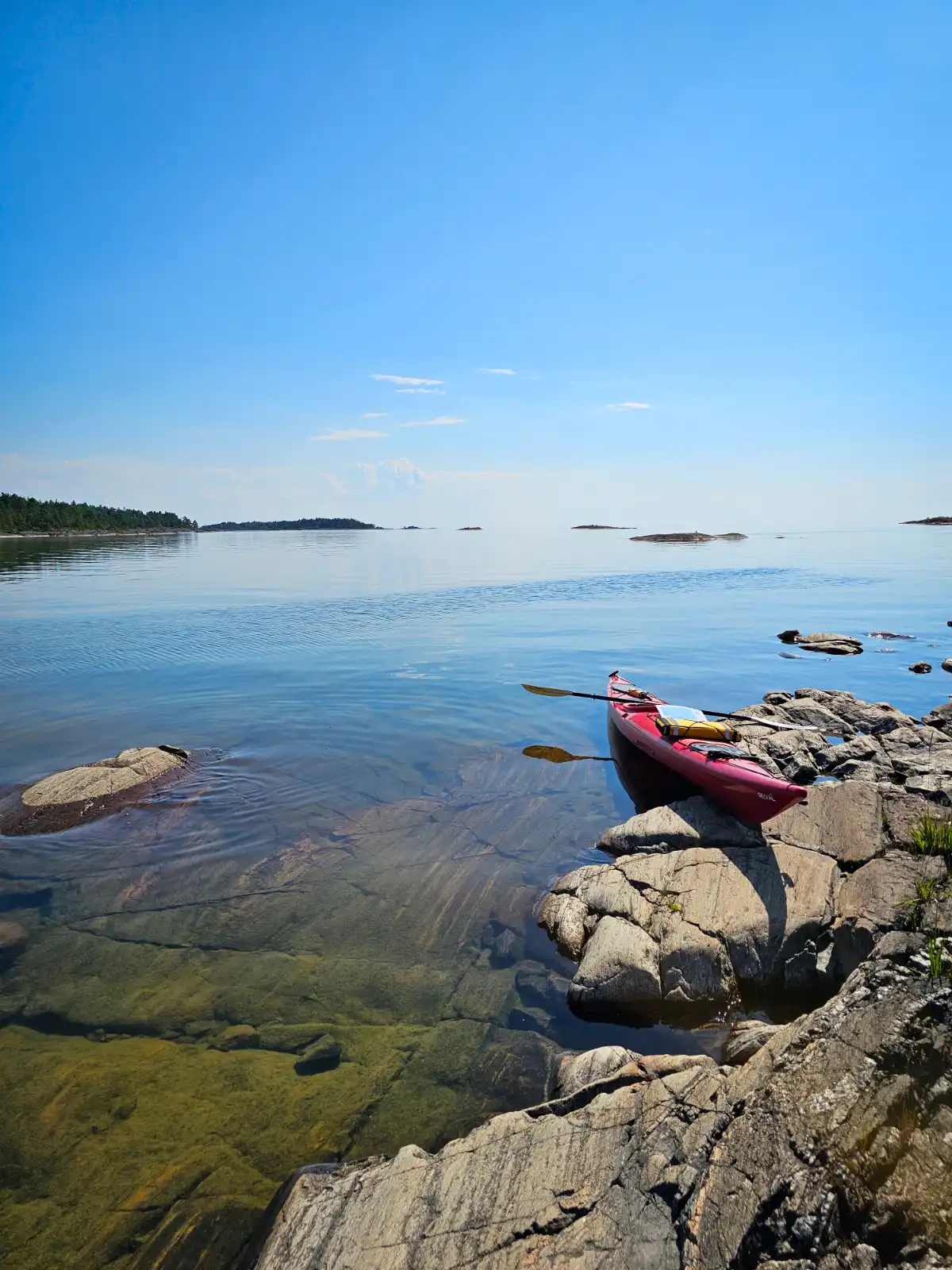 Alt-text: Utsikt över Ekenäs gästhamn och camping med båtar förtöjda vid bryggan och ett stilla vatten som sträcker sig mot horisonten. I bakgrunden syns kustlinjen och omgivande natur.