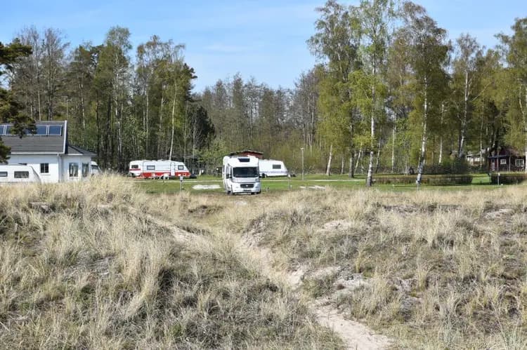Bild av en campingplats på Sudersand Resort med flera husvagnar och husbilar parkerade på öppna gräsytor. I bakgrunden syns vidsträckta ängar och en klar blå himmel.