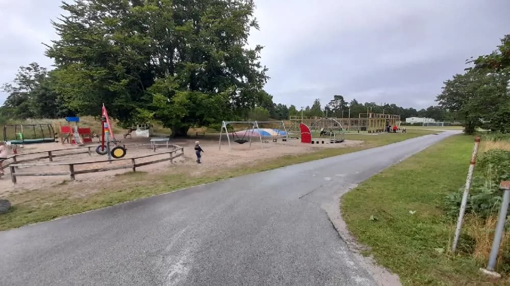 En solig dag på Sudersand Resort, där barn leker i en park med utomhuslekutrustning under en klarblå himmel med spridda moln.