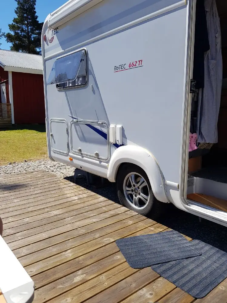 En campingplats med husvagn och husbil parkerade på gräsytor, omgivna av träd och natur.