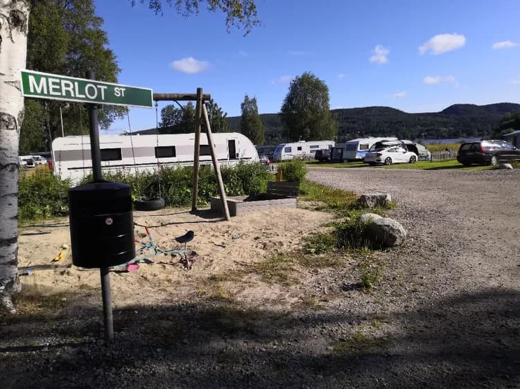 En husvagn och flera fordon parkerade på en campingplats, omgivna av grönska i en fridfull miljö.