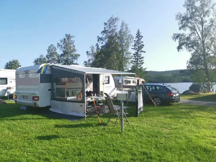 En bild av Snibbens Camping som visar husbilar och husvagnar parkerade på grönområdet. En tältplats och campingstolar är synliga, vilket ger en inblick i de tillgängliga faciliteterna för besökare.
