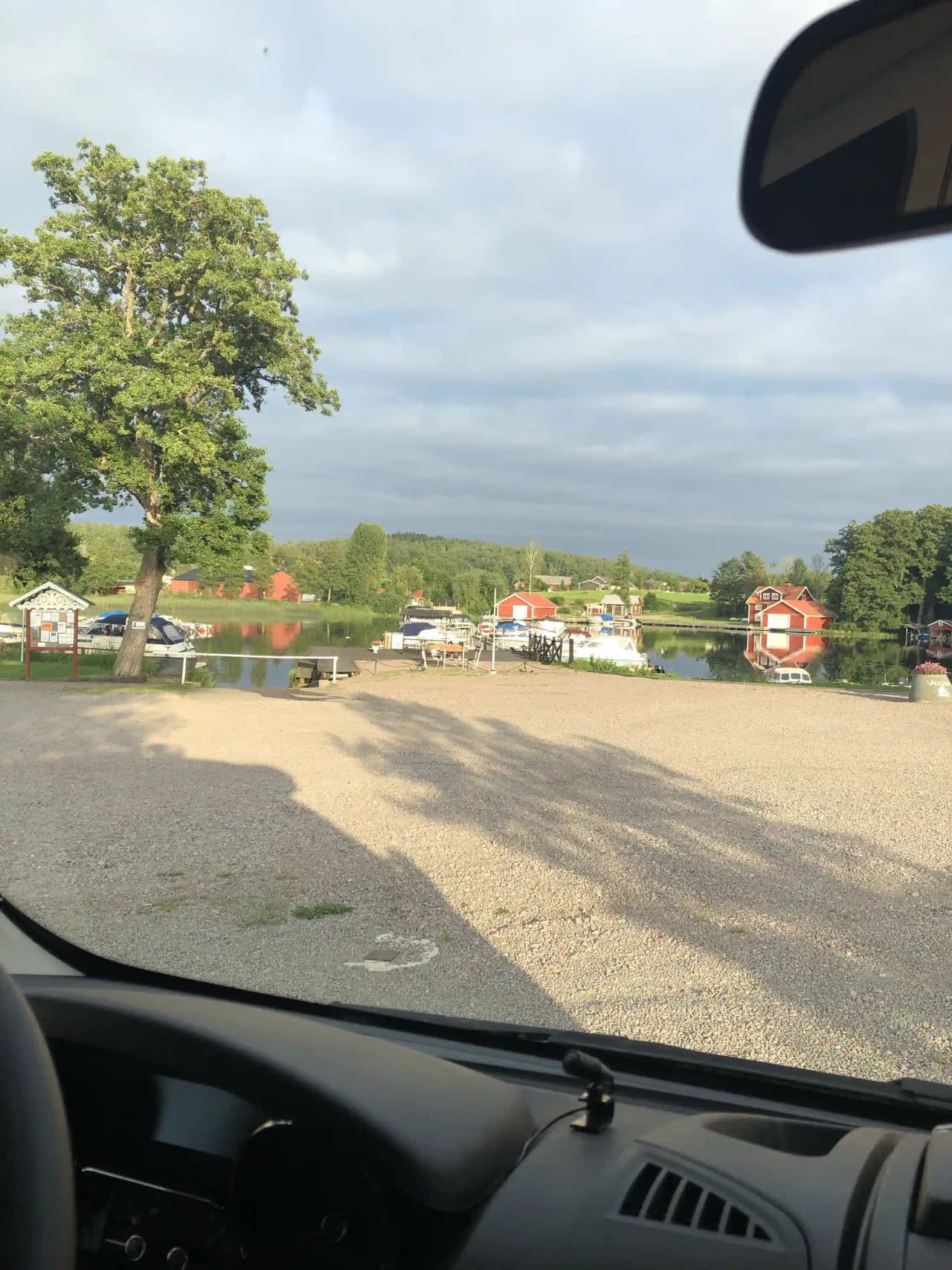 En bil kör längs en naturskön väg med molnig himmel. Föraren har en klar vy genom vindrutan som är utrustad med vindrutetorkare. Backspeglar syns på bilden, vilket bidrar till känslan av en pågående bilresa.