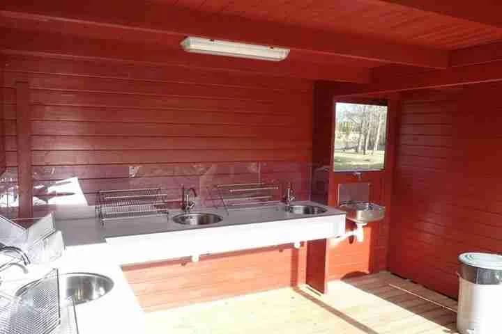 En träbyggnad med dörr, liknande en timmerstuga, omgiven av natursköna omgivningar, vilket representerar en del av campingområdet på Alevi.