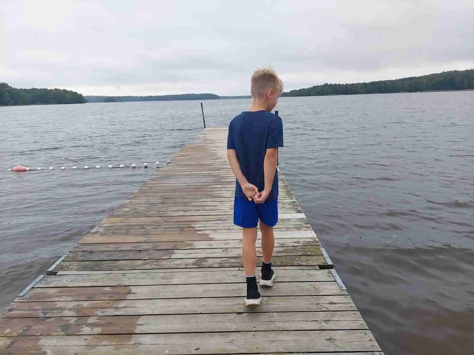 En grupp människor njuter av sommaren på Luhrsjöbadens camping. De är klädda i sommarkläder och spenderar tiden vid en brygga intill sjön. Stämningen är avslappnad och glädjefylld, typisk för en semester vid vattnet.