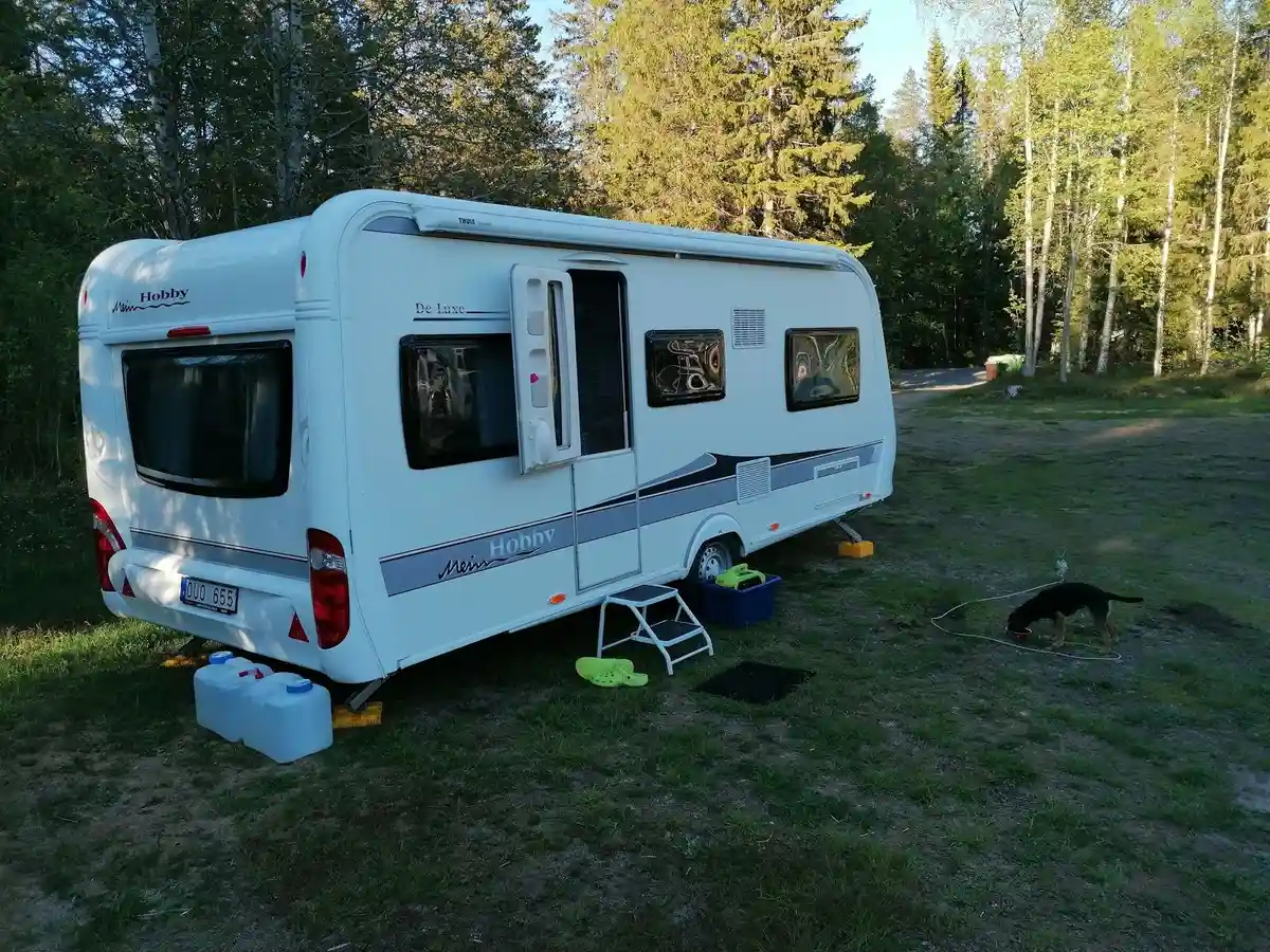 En husvagn står parkerad på Storsands camping, omgivet av grönskande natur.