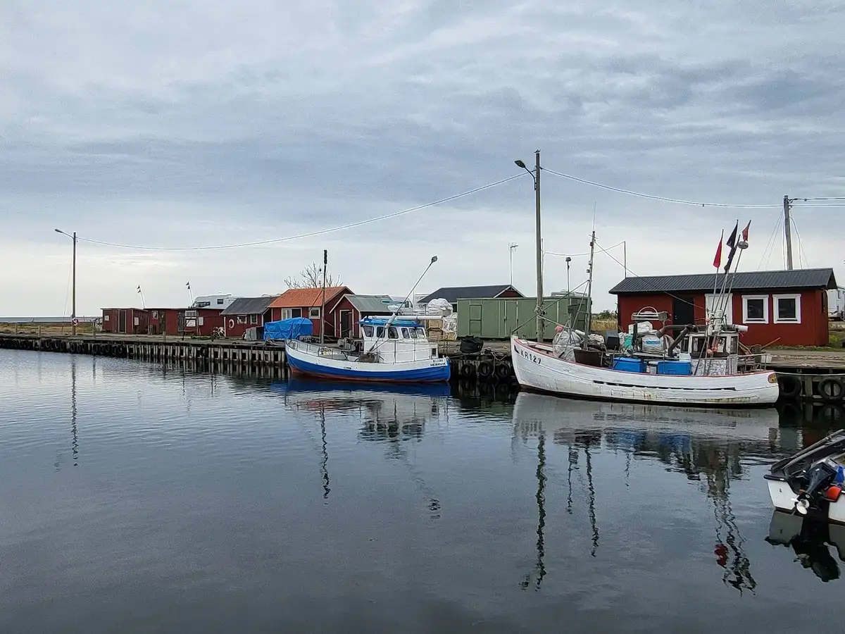 En båt ligger förtöjd vid en brygga i en stilla hamn vid Valjevikens camping, omgiven av klart vatten och grönskande stränder i bakgrunden.