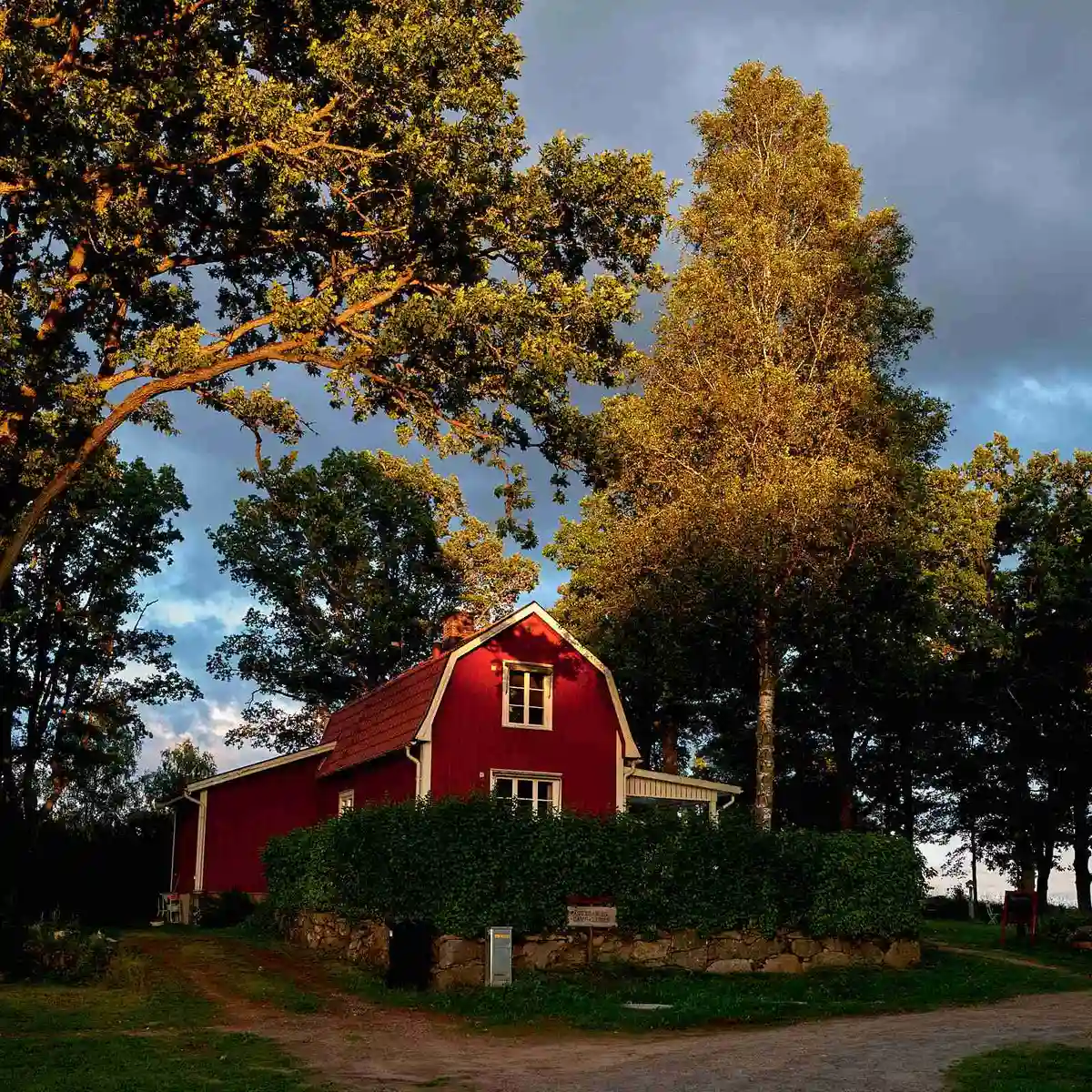 En stuga omgiven av frodig grönska med blad, grenar och buskar i vårsolens ljus, del av Agundaborg Camp & Paddle. En välskött gräsmatta och trädgårdslandskap kompletterar den natursköna miljön.