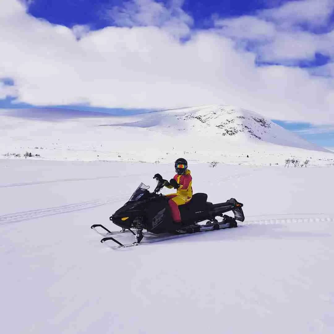 En snöskoter kör över ett snötäckt landskap vid sportcampingen i Åkersjön, omgivet av berg och glaciärer i vinterskrud.