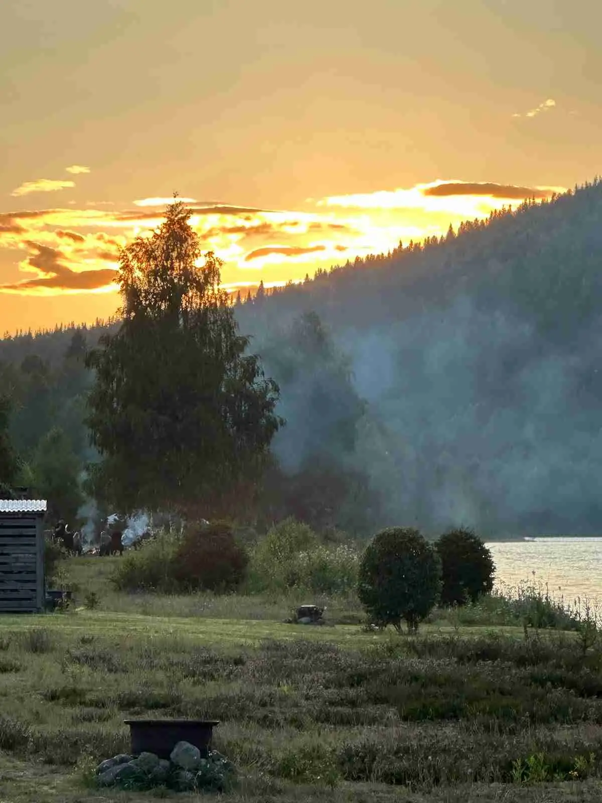 En vy över Bråtens camping med bergiga landskap och grönskande kullar i bakgrunden. Det är sommartid och naturen är i full blom under en klar himmel.