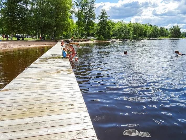 En rofylld utsikt över en sjö vid Alsterbro camping, med en brygga som sträcker sig ut över vattnet och reflektioner av det omgivande landskapet. Perfekt för rekreation och avkoppling under semestern.