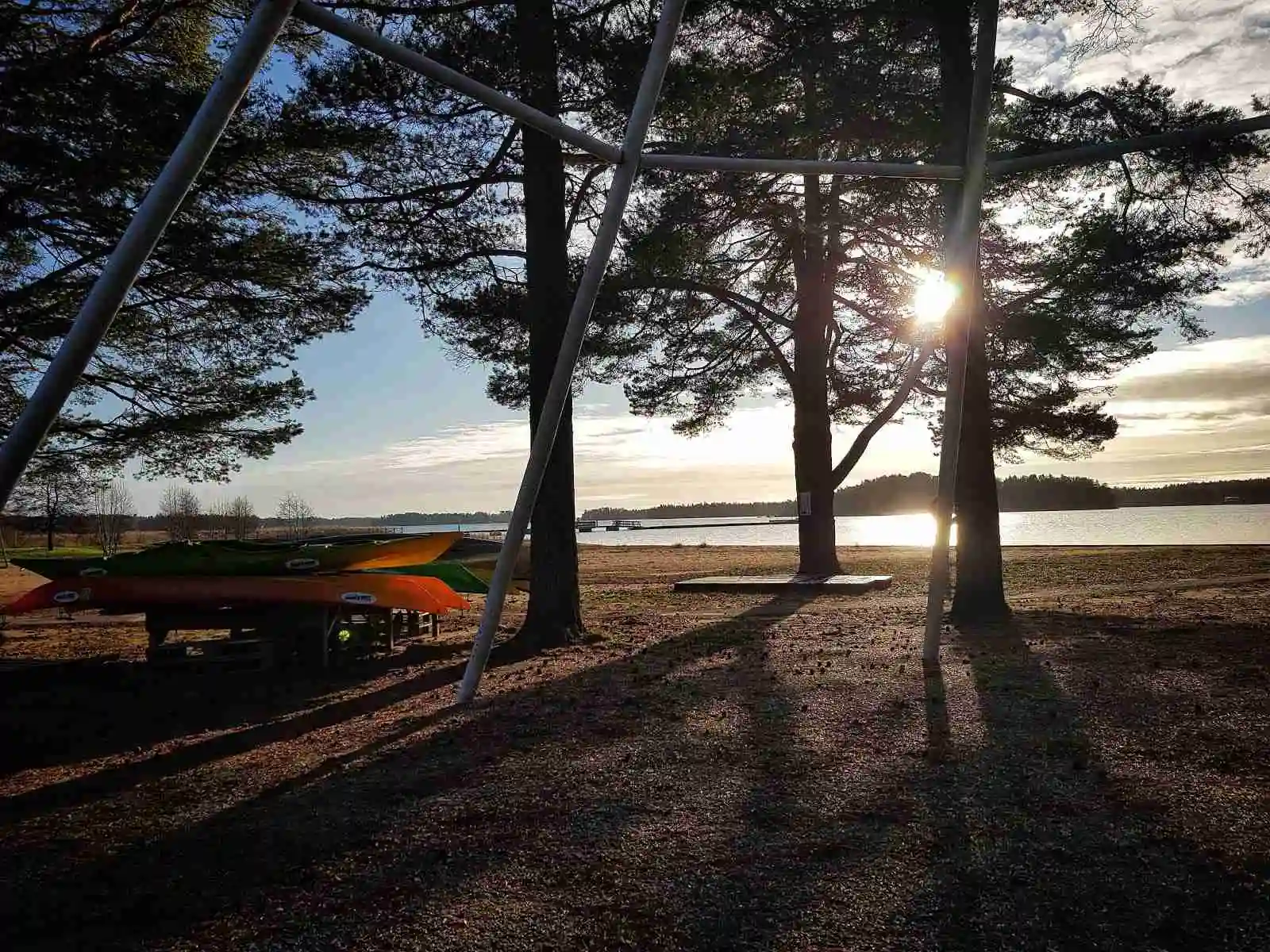 En lugn strand med trädgrenar som siluetter mot en färgglad solnedgång vid Stenö havsbad & camping.