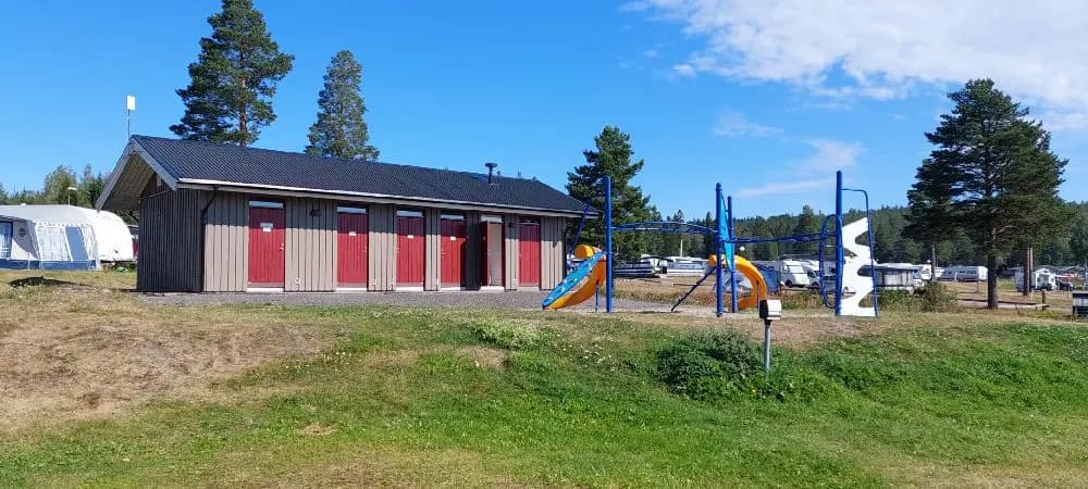 En grönskande campingplats vid Gullviks Havsbad med stugor och ett skuggigt område i närheten. En välskött gräsmatta omgiven av träd ger en inbjudande atmosfär för besökare.