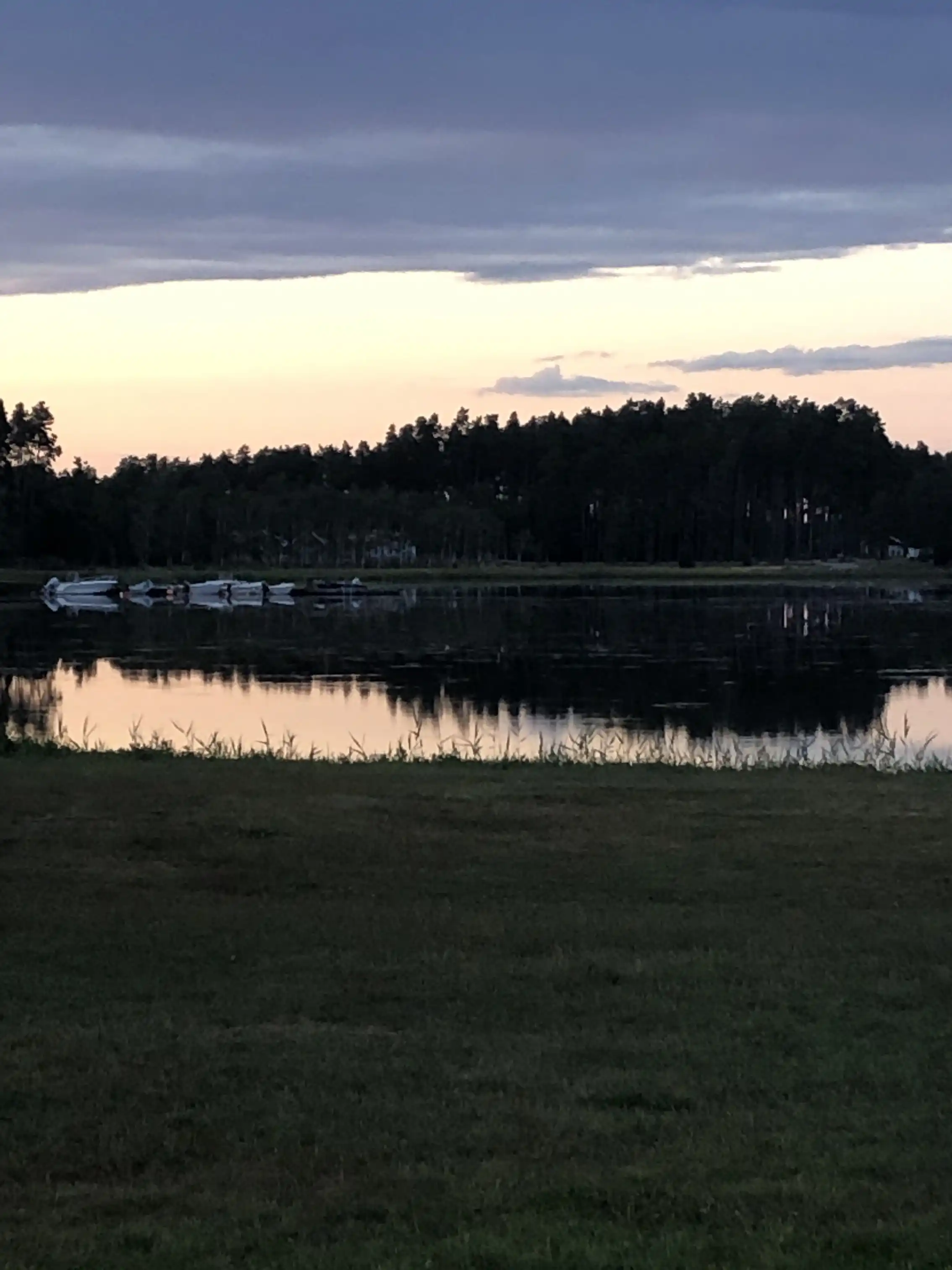 En lugn kvällsbild vid Skeppeviks camping, där himlen färgas av skymningen över horisonten. Vatten och vidsträckt natur skapar en fridfull stämning i det naturliga landskapet.