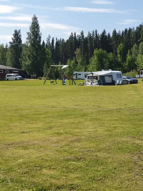 Bild av campingplatsen JanneSland med grön gräsmatta, träd och öppet landskap.