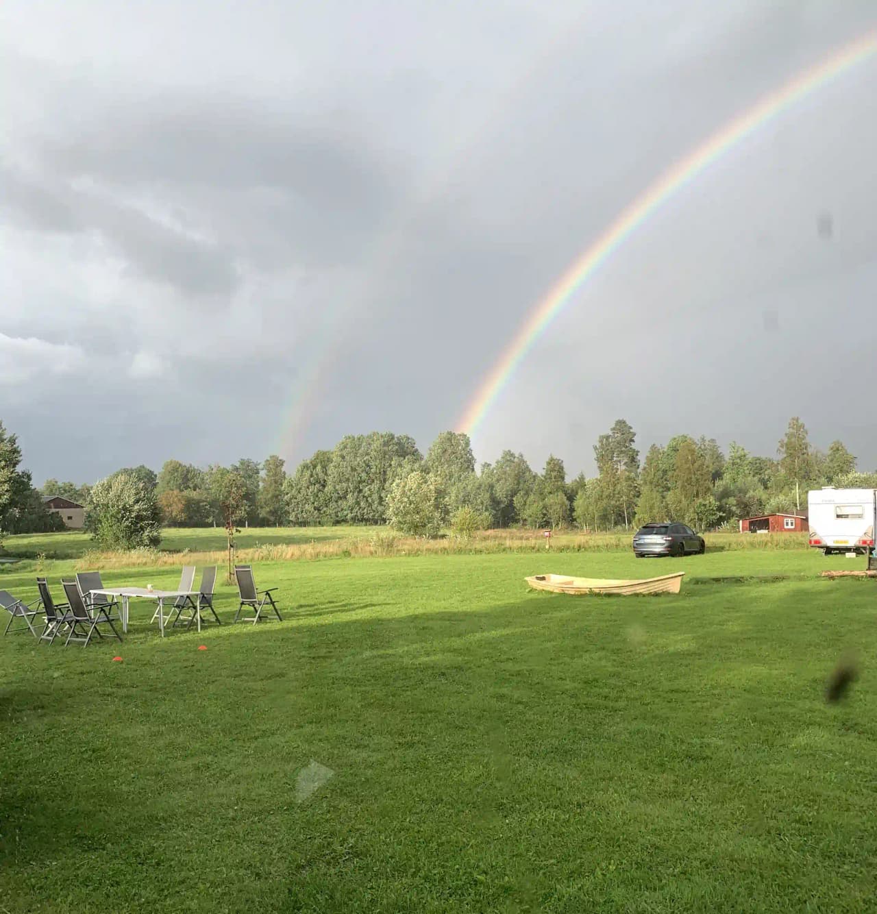 En vidsträckt landskapsscen från Abrahams Camp med ett böljande gräsfält och låg vegetation under en klar himmel, där en regnbåge sträcker sig över landskapet.