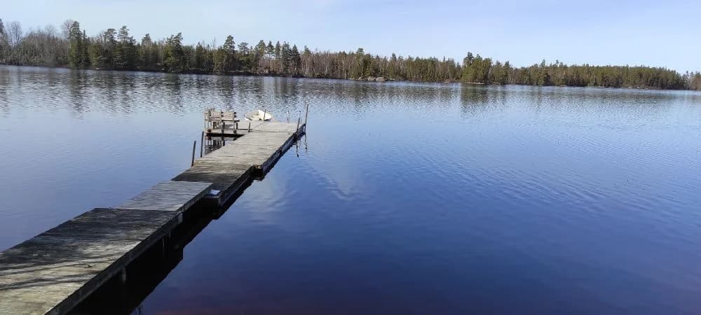En lugn vattenspegel omgiven av grönska vid Abrahams Camp, med blå himmel reflekterad i vattnet.
