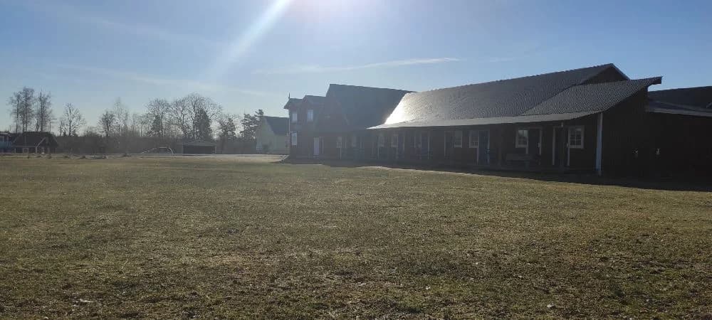 En lantlig stuga med träfasad och sluttande tak, omgiven av en öppen gräsyta och mark.