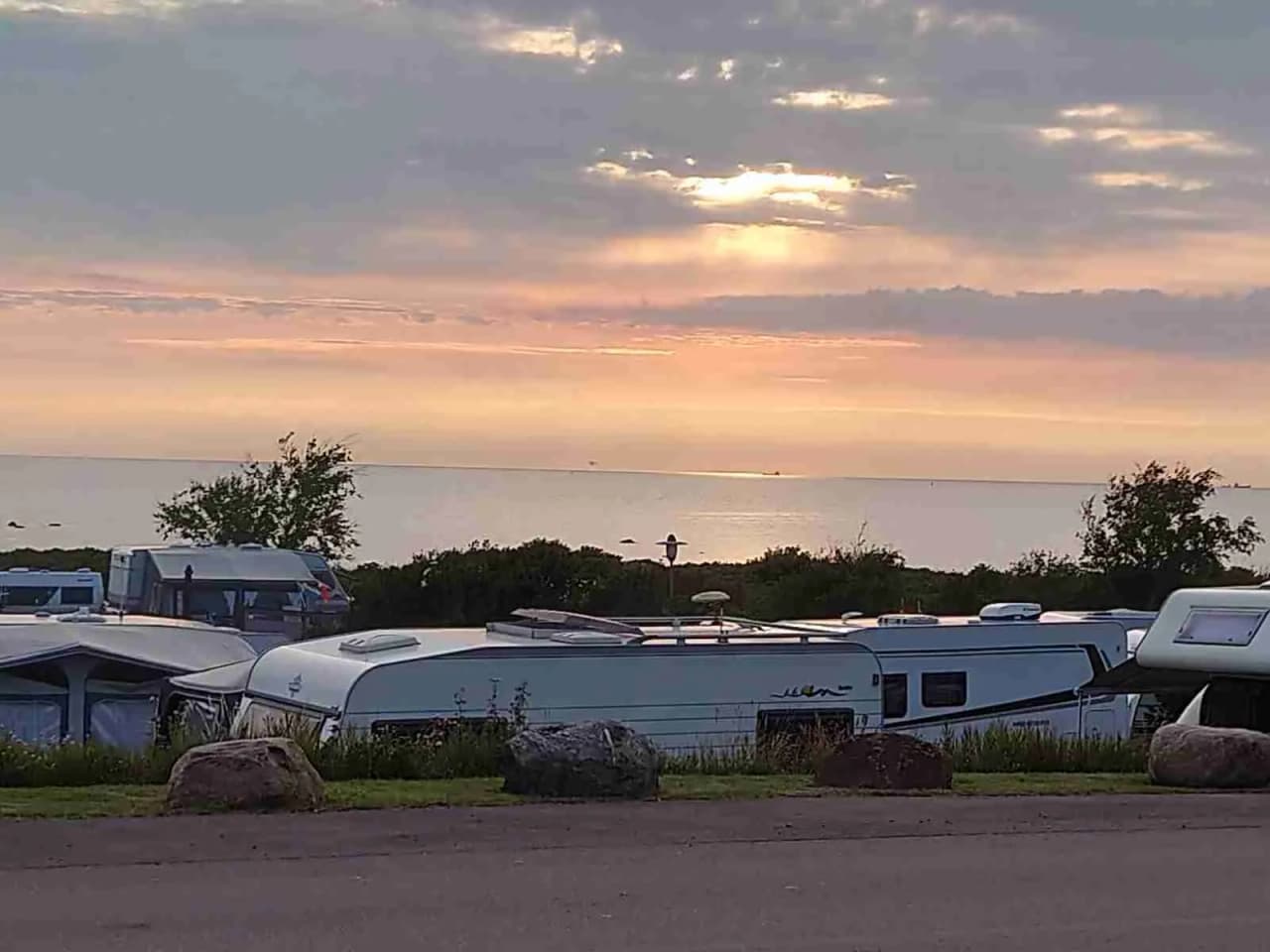 En husbil står parkerad på Lerbergets Camping under en vacker solnedgång, med moln på himlen och en nästan tom parkeringsplats i skymningen.