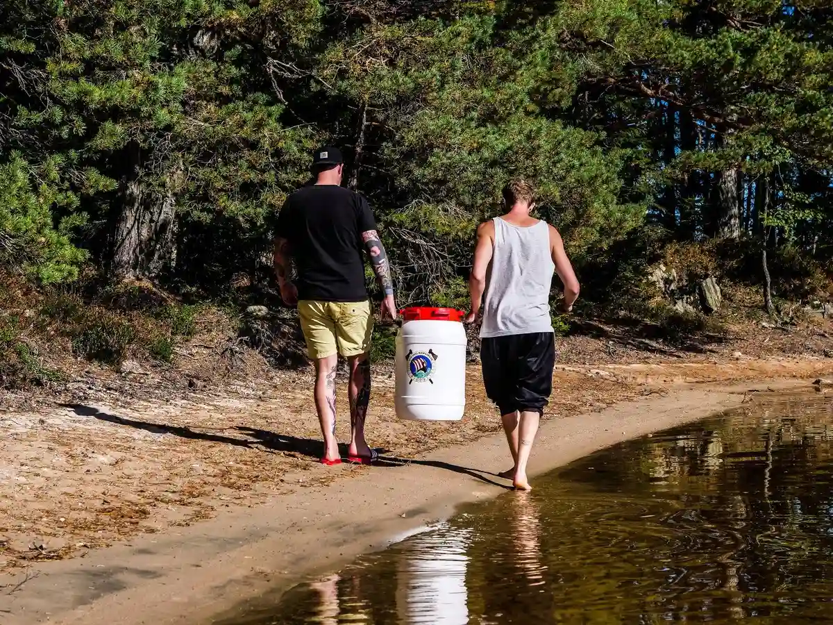 En grupp människor njuter av sin semester på en sandig strand vid Viking Republic Nature Camp, omgivna av natur och glädje. I förgrunden finns en hink som en del av deras strandaktiviteter.