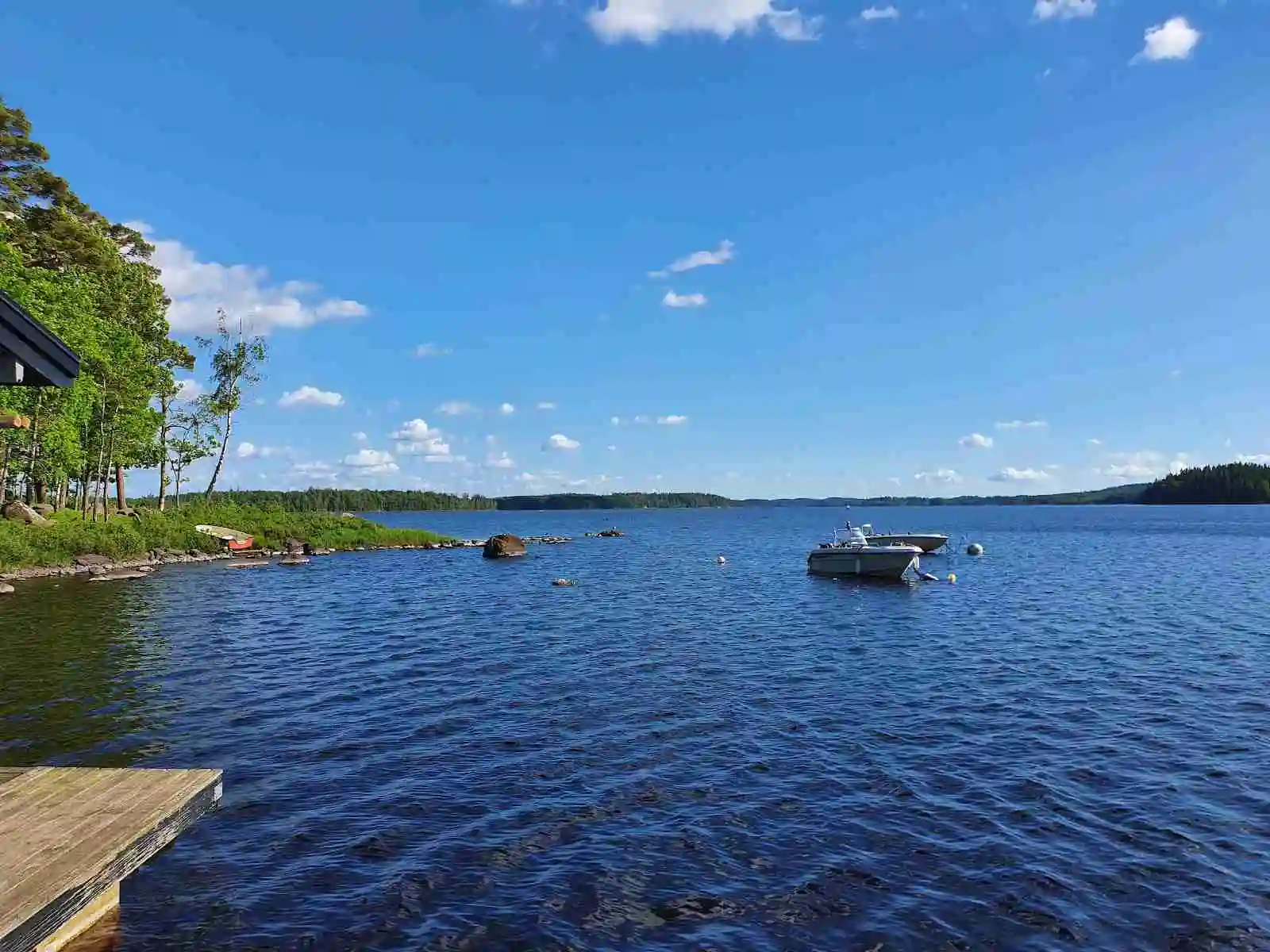 En somrig vy över Kalvs Familjecamping visar en vidsträckt blå sjö omgiven av grönskande natur och en strandlinje som lockar med sol och rekreation.