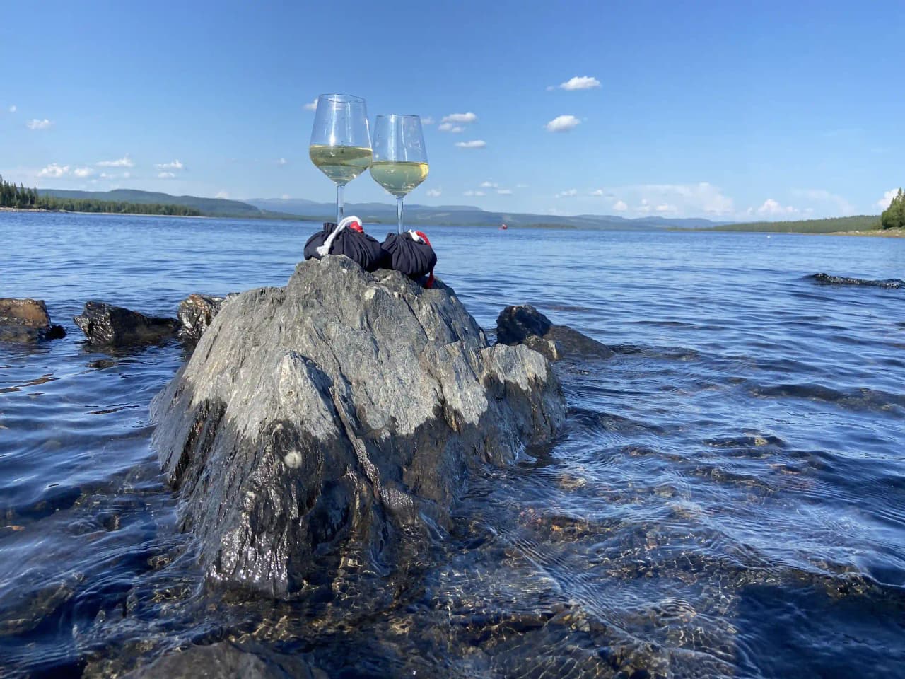 Vy över en naturskön sjö med omgivande kustlandskap vid Kallsedet Camping. Stillastående vatten omges av grönskande skogar och berg i horisonten.