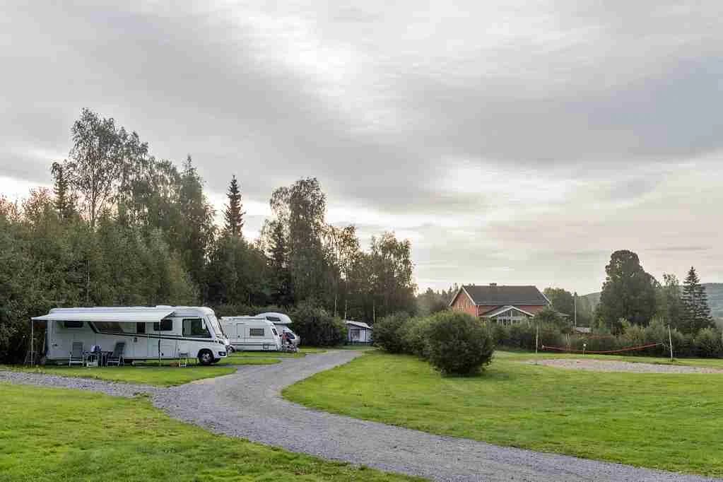 En familjebil och en kompakt SUV parkerade på en gräsmatta nära en park, omgivna av träd och öppet utrymme.