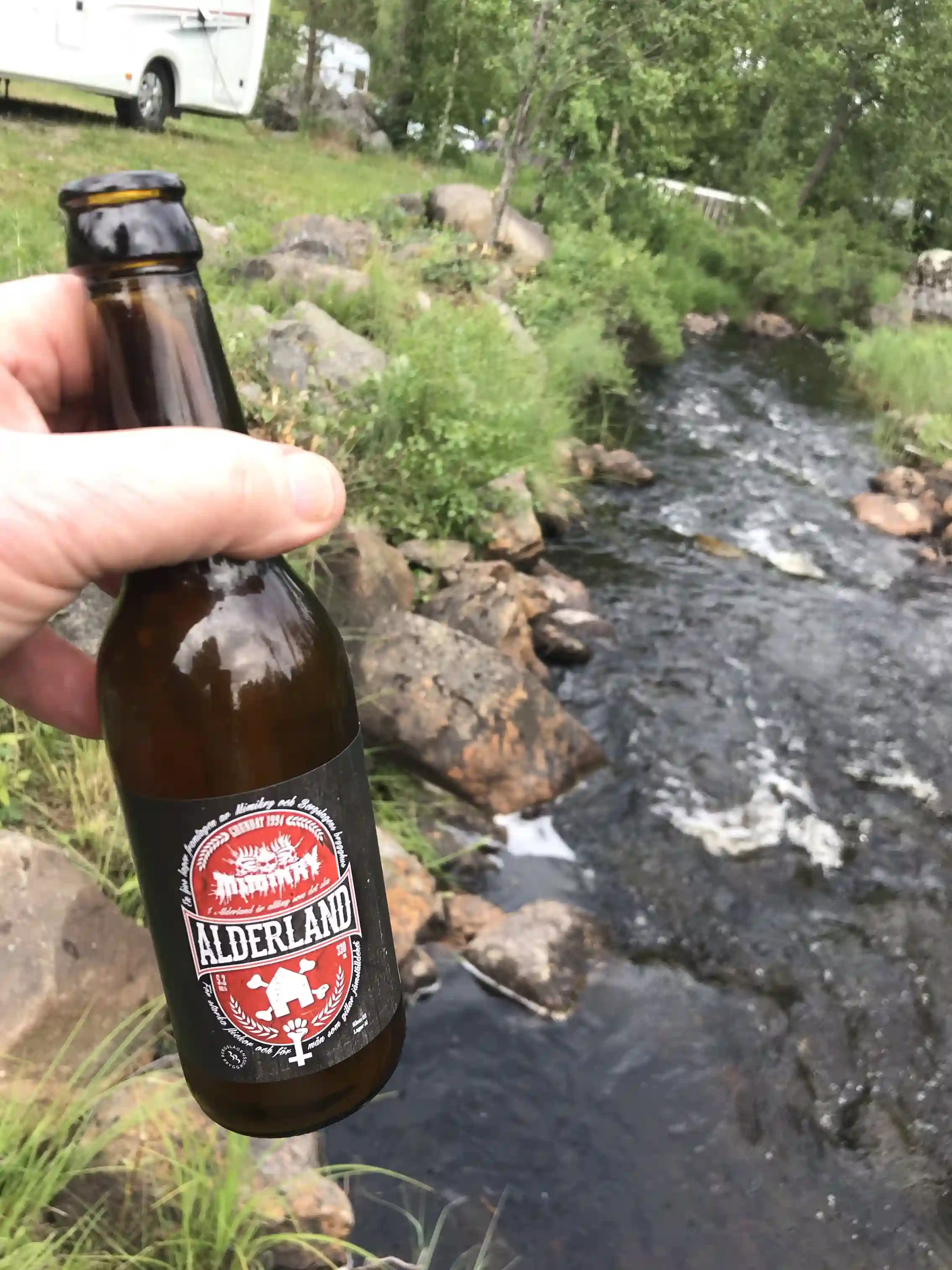 En bild av en glasflaska med öl, stående på ett bord på Skärså camping. Bakgrunden visar en naturskön campingmiljö, vilket ger en avslappnad atmosfär.