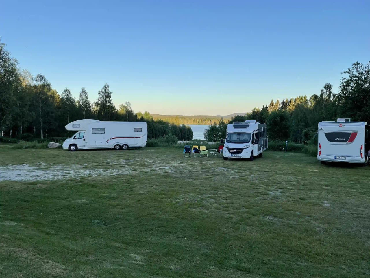 Bild på en husvagn och flera bilar parkerade vid Storsjö Camping & Trädgård. Området är avsett för camping och rekreation, med olika fordon synliga på platsen.