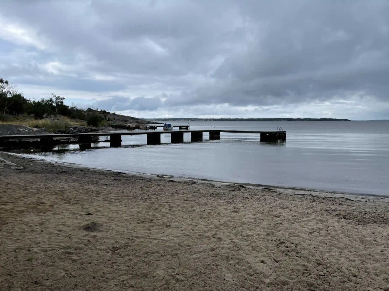 En vy över ett lugnt vattenlandskap med en horisontlinje där himmel möter hav. Kusten kantas av en mjukt böljande strandlinje.