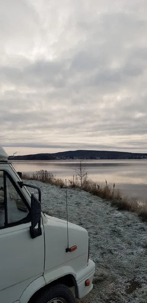Bild av en parkerad bil vid Arvika småbåtshamn, med en utsikt över vattnet och båtar i bakgrunden. En solig dag med klar himmel och omgivande grönska.