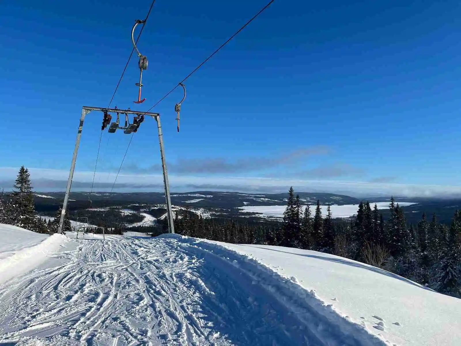 Snötäckt vinterlandskap vid sportcamping Åkersjön med bergskedja i bakgrunden, perfekt för rekreation och skidåkning i de pistade sluttningarna.