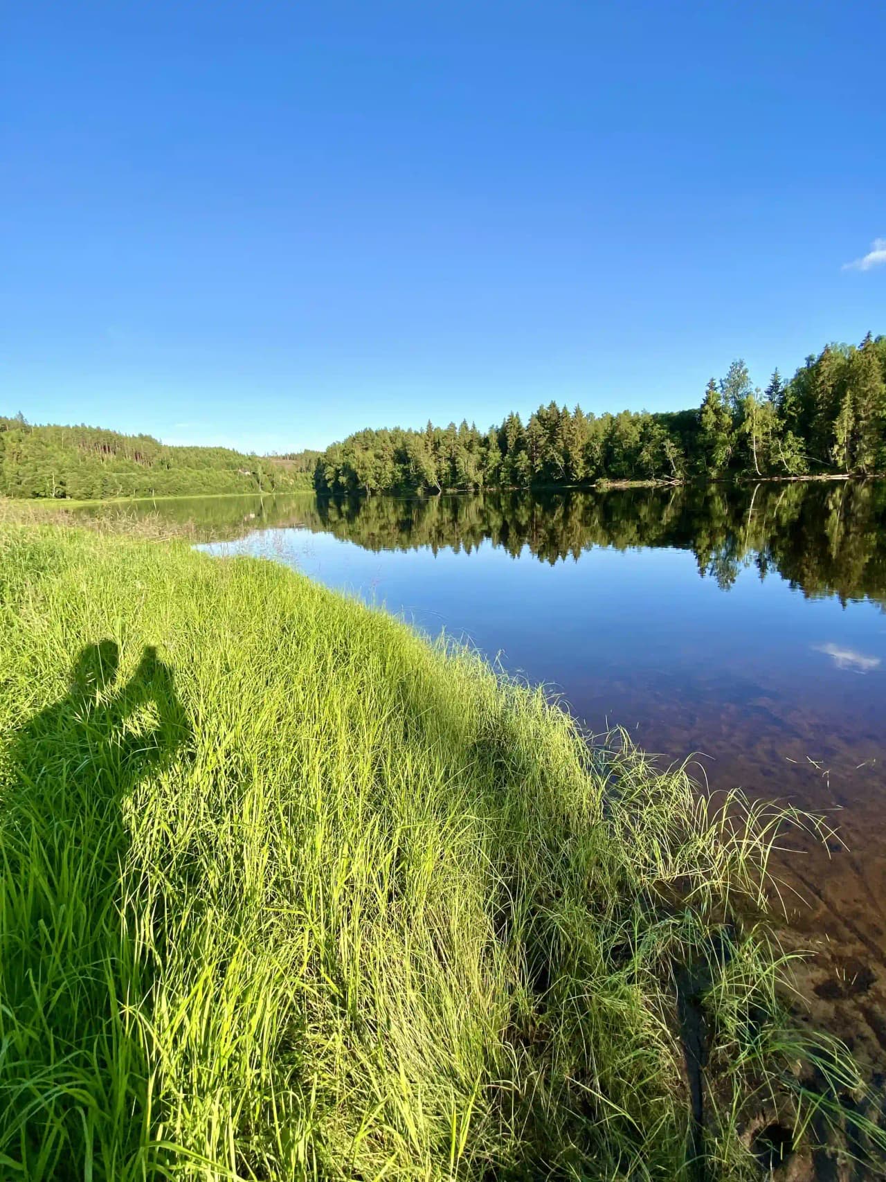 Vy över Björkebo Camping med klarblå himmel, gröna omgivningar och en glittrande vattensjö, som fångar den fridfulla sommaridyllen.