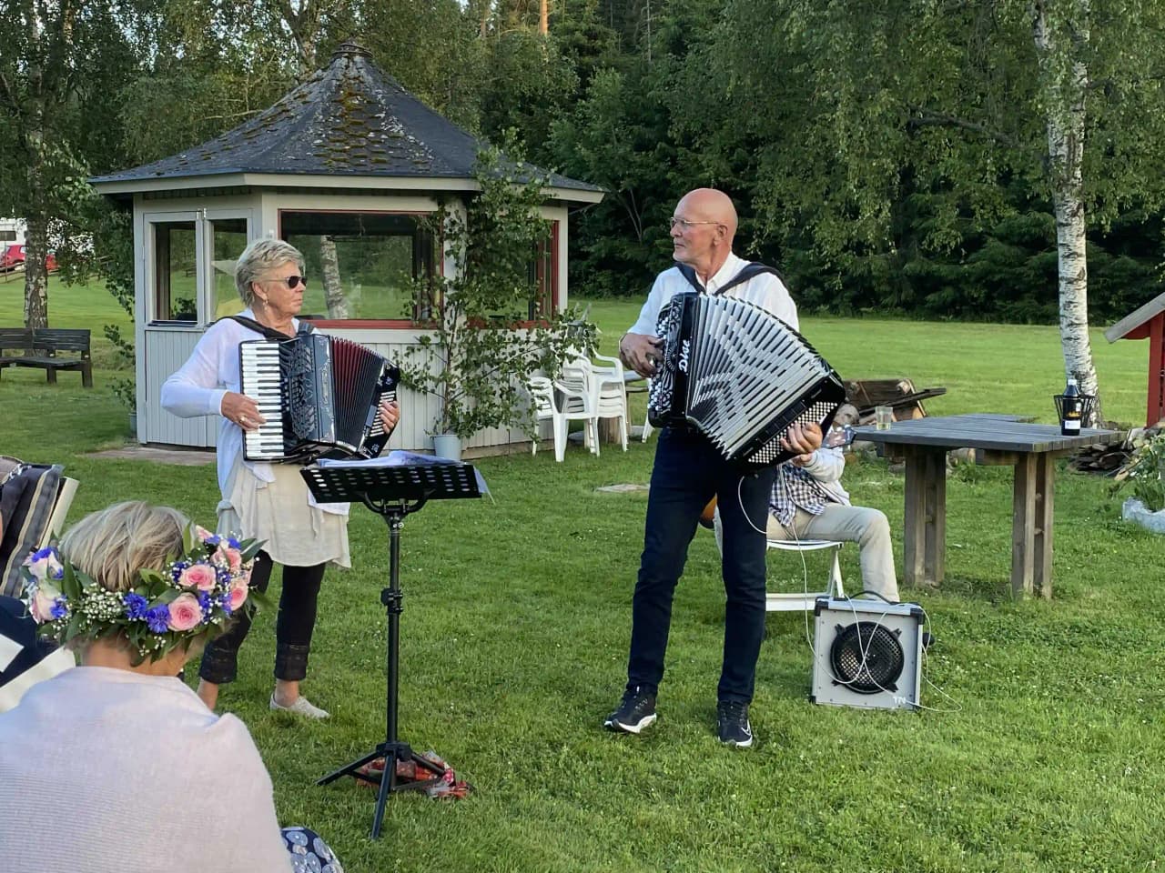 En musiker spelar dragspel utomhus på Svennevads camping, omgiven av en avspänd och avslappnad atmosfär med andra campinggäster i bakgrunden.
