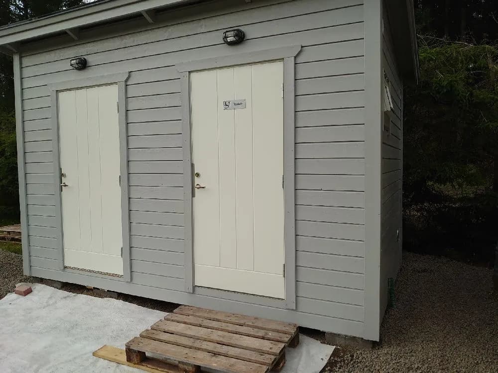 En grå träbyggnad på Svennevads camping med robusta trämaterial, inklusive plankor och träpaneler. Byggnaden ser ut som en liten stuga eller skjul i en naturlig miljö.