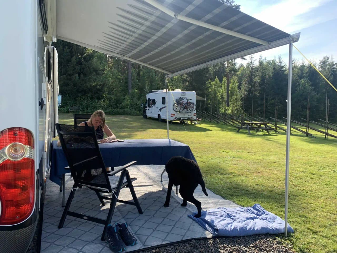 En husvagn står under ett solskydd vid Svennevads camping, omgiven av träd och natur.