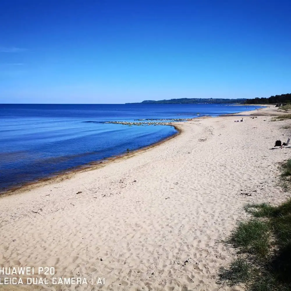 Vy över en sandstrand vid ängdala camping på Österlen, med blått hav och en vidsträckt horisont i bakgrunden.