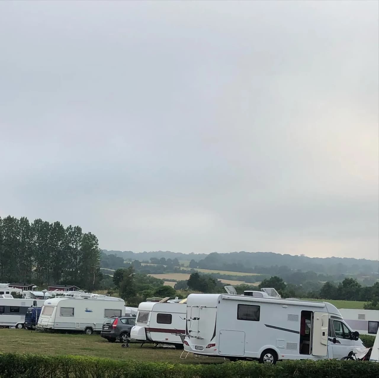 En campingplats på Österlen med flera husbilar och husvagnar parkerade på en grusplan under en himmel med vita moln.
