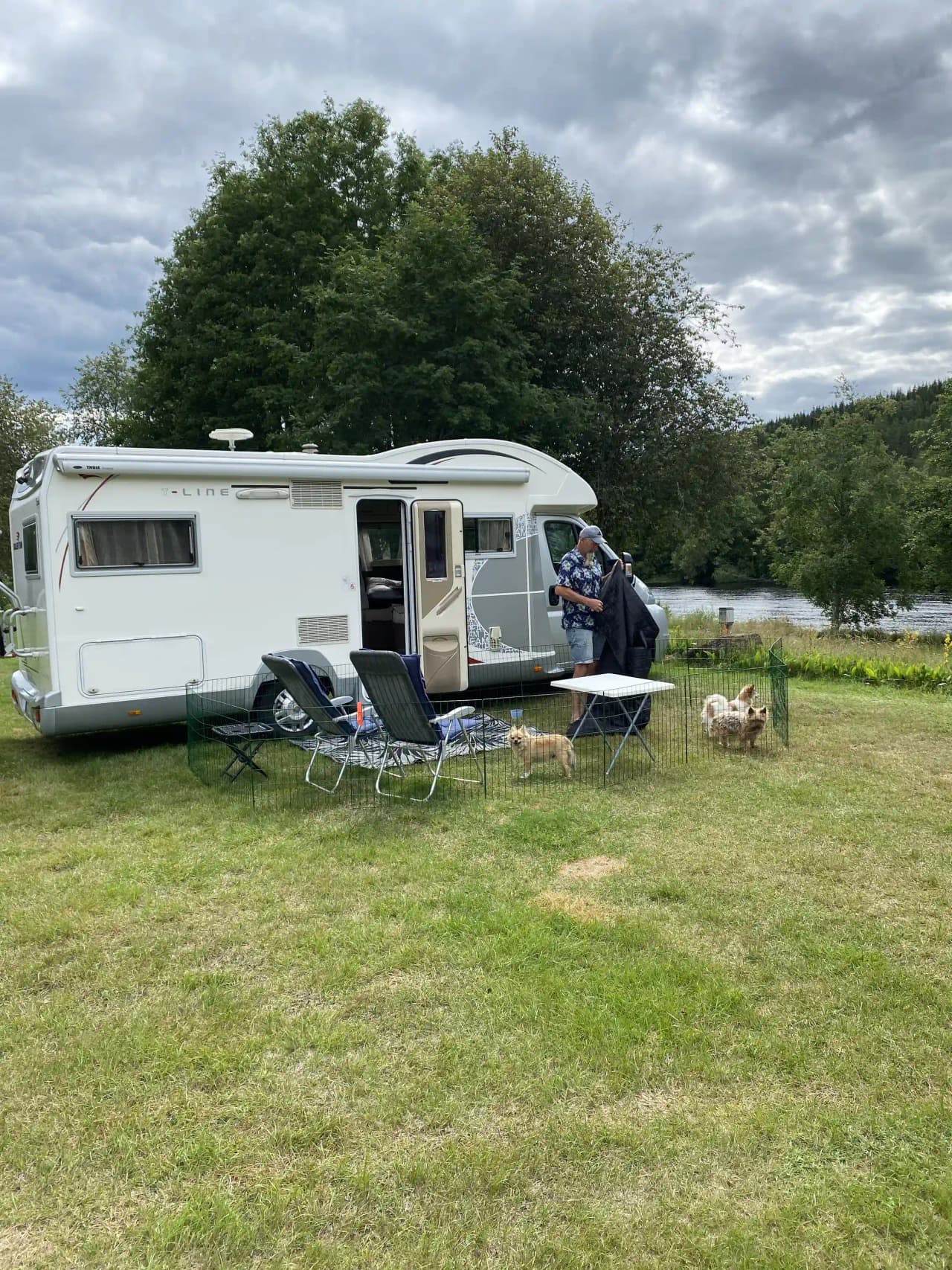 En campingplats med flera husbilar och husvagnar parkerade på en grön gräsmatta, omgiven av träd, vid Värnäs Camping.