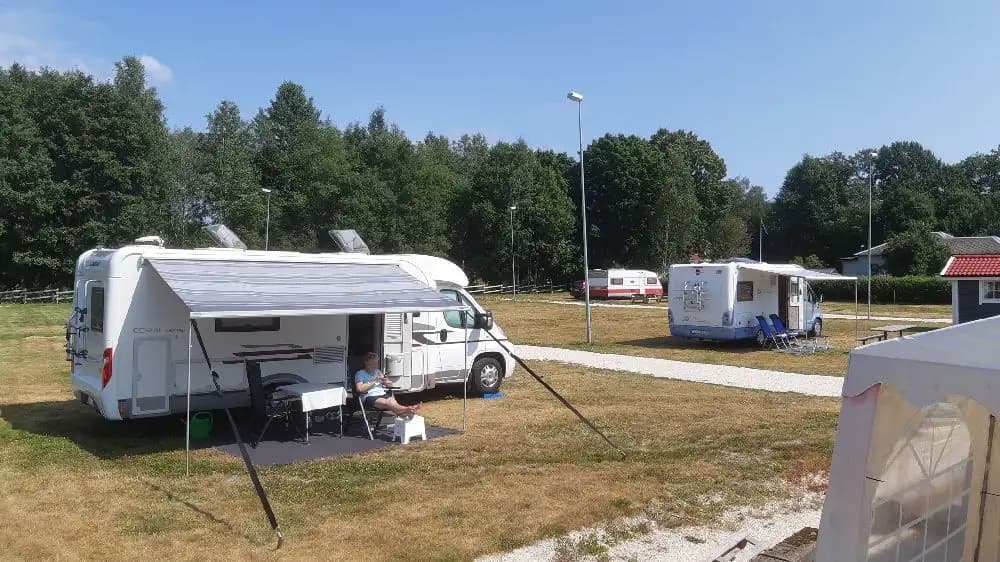 En campingplats med flera husvagnar och husbilar parkerade på grusplatser. Området är omgärdat av träd och erbjuder plats för olika typer av fritidsfordon.