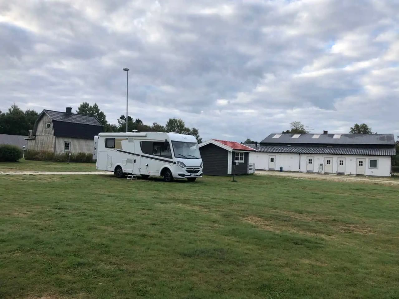 En bild av Kerstins Camping som visar flera husvagnar och husbilar parkerade på en grön gräsmatta. I bakgrunden syns en uppfart och ett garage. Området verkar vara välvårdat och inbjudande för campingbesökare.