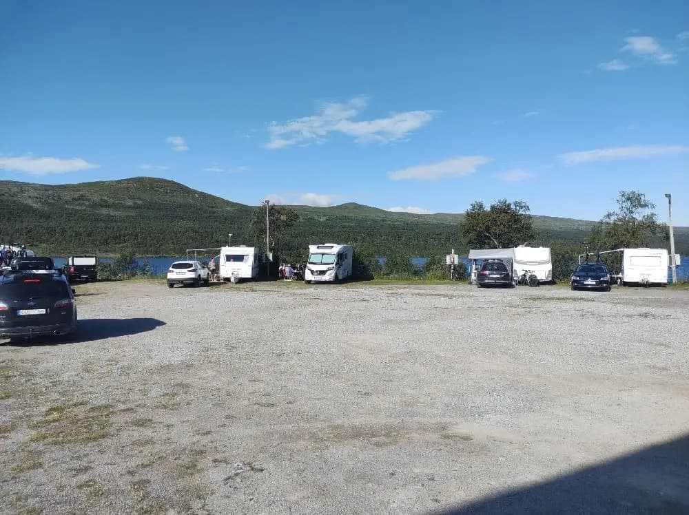 Alt-text: En parkeringsplats vid Fjällnäs camping med flera bilar uppställda under en molnig himmel.