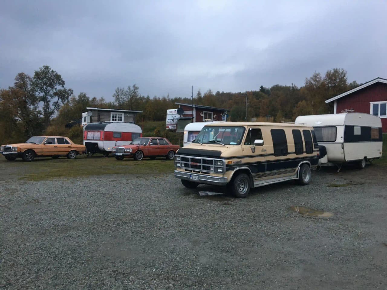 En campingplats i fjällmiljö, med parkerade fordon inklusive bilar och husbilar.