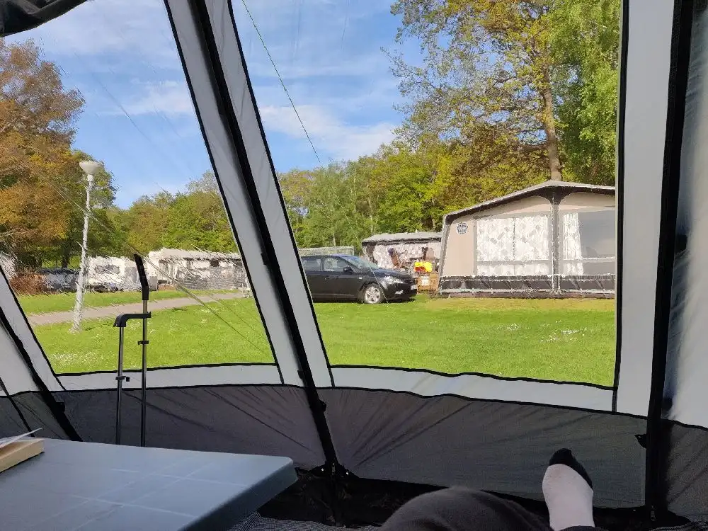 En campingplats med tält under skuggan av ett träd, med en presenning som kan användas som skydd mot solen.