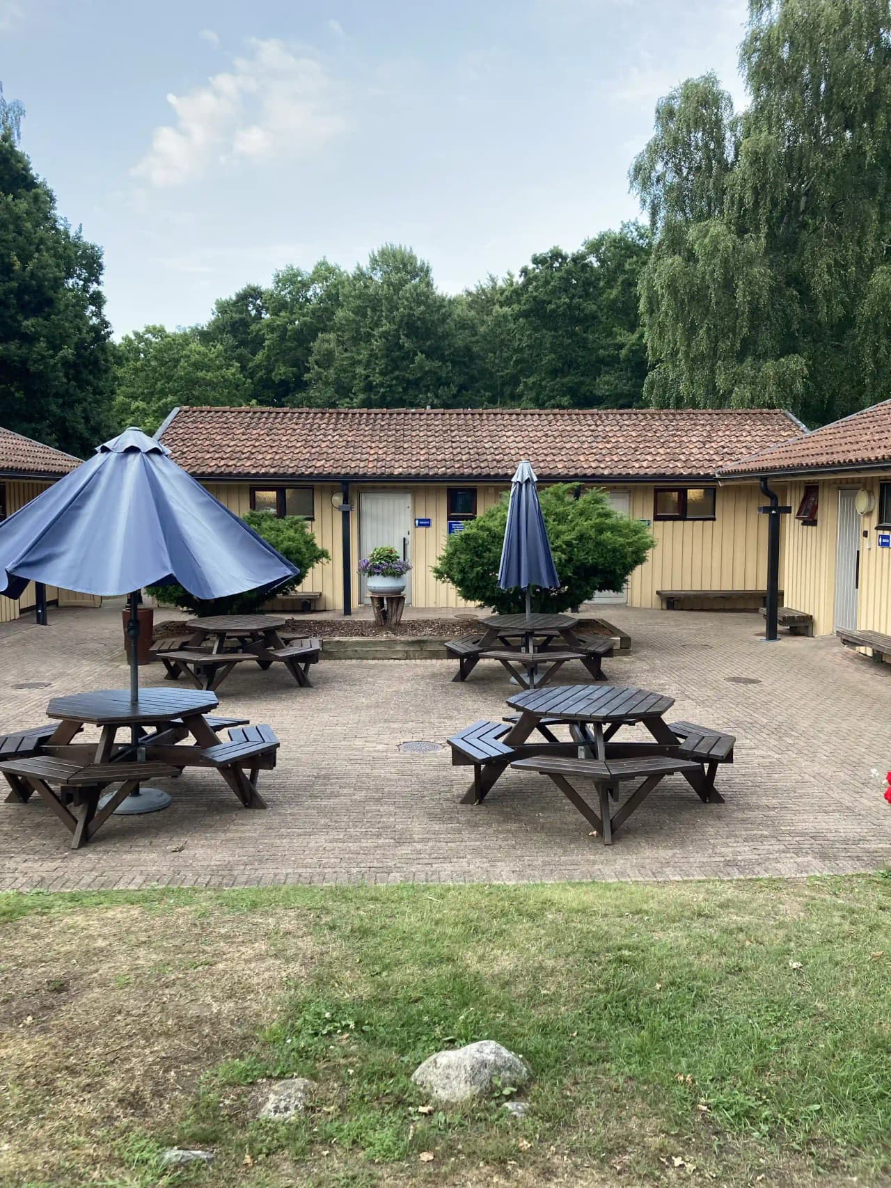 En bild av ett uteområde vid Järnaviks camping med utemöbler och picknickbord, omgiven av skuggande träd och grönska, som skapar en inbjudande atmosfär för mat och samvaro utomhus.